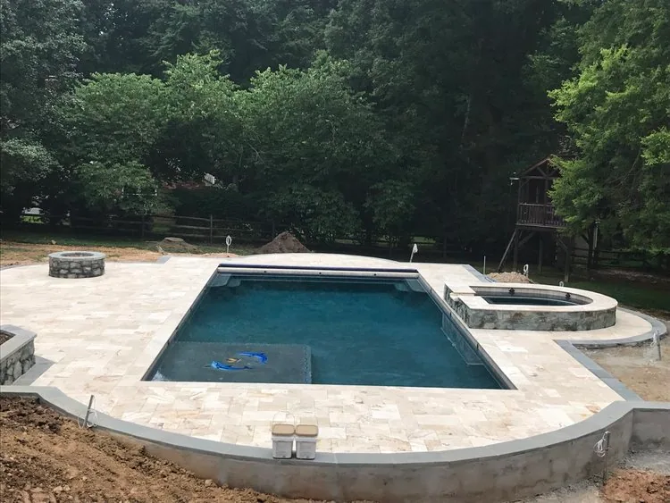 Swimming pool and rounded spa surrounded by stone paving and mature trees