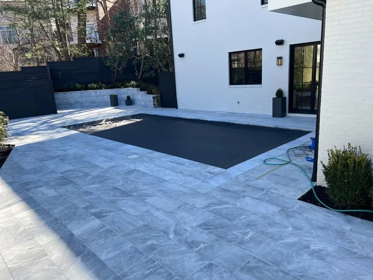Gray pool surround and a protected swimming pool beside a white home