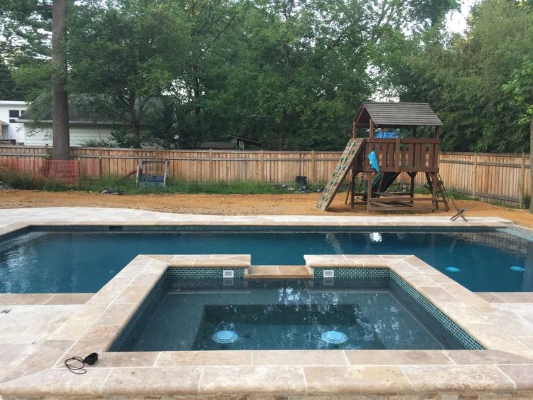 Square spa integrated into the stone surround of a backyard swimming pool