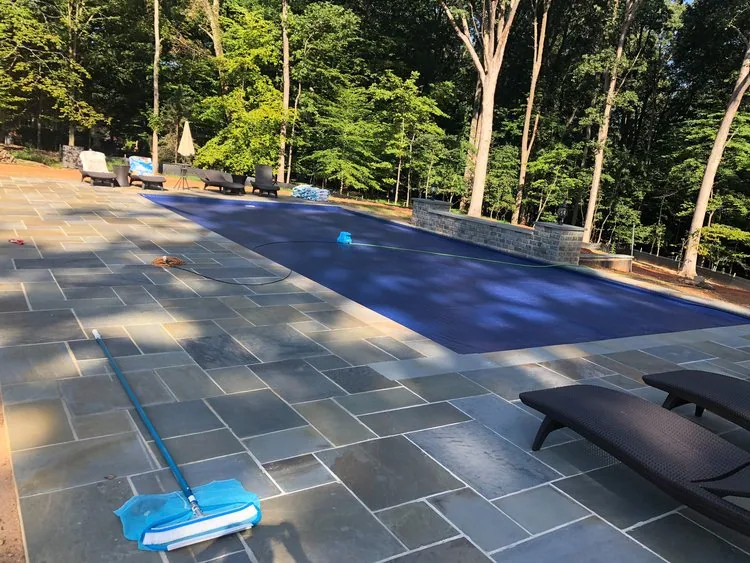 Swimming pool covered for protection with a surrounding stone patio under leafy trees