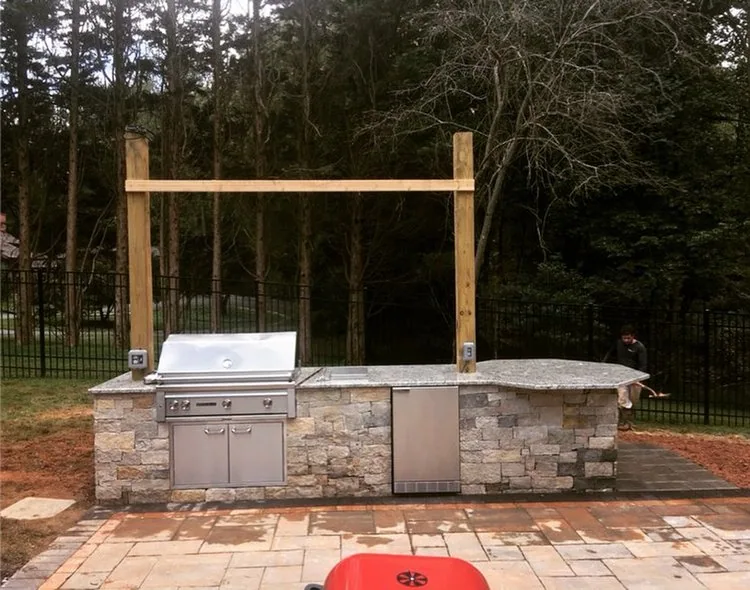 Stone outdoor cooking area with a built-in grill and a timber frame above