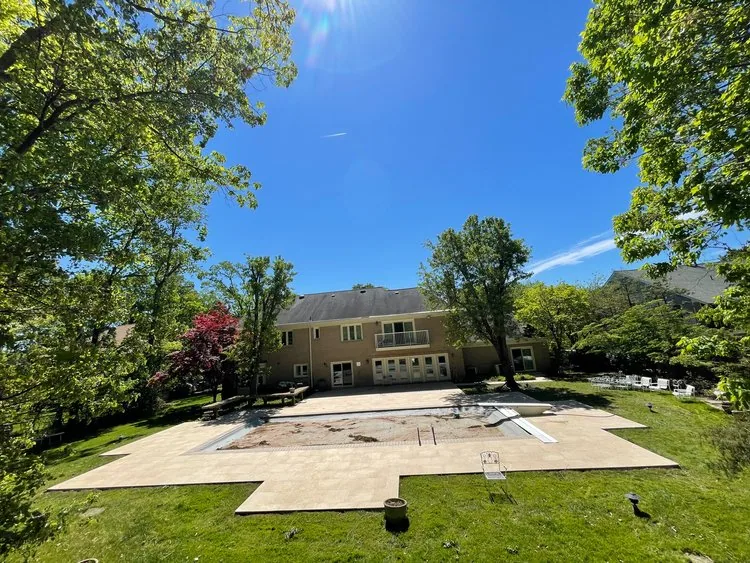 Wide view of a backyard pool terrace framed by a lawn and mature trees