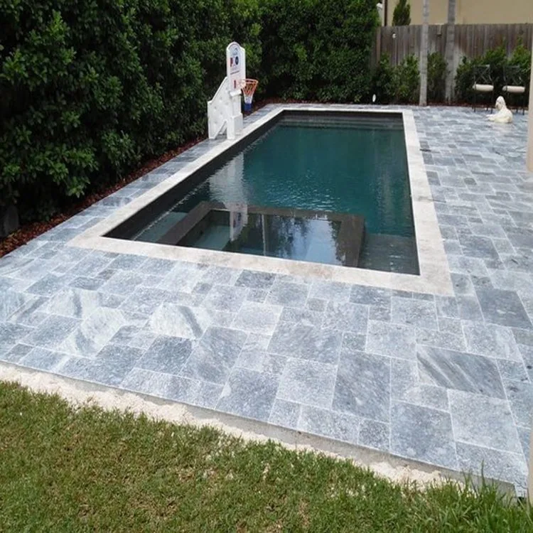 Rectangular swimming pool and gray stone patio bordered by trees