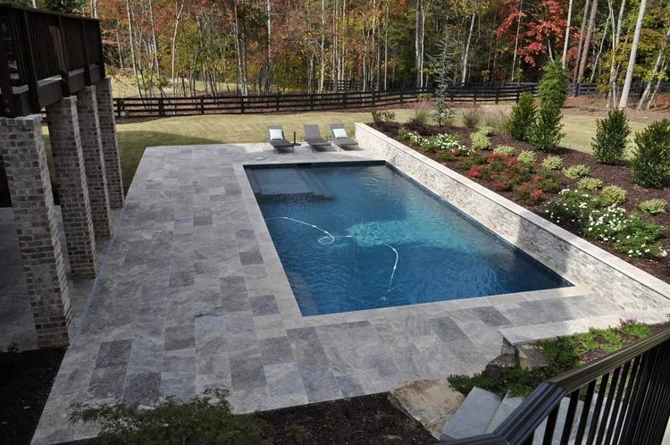 Rectangular pool surrounded by gray stone paving and backyard greenery