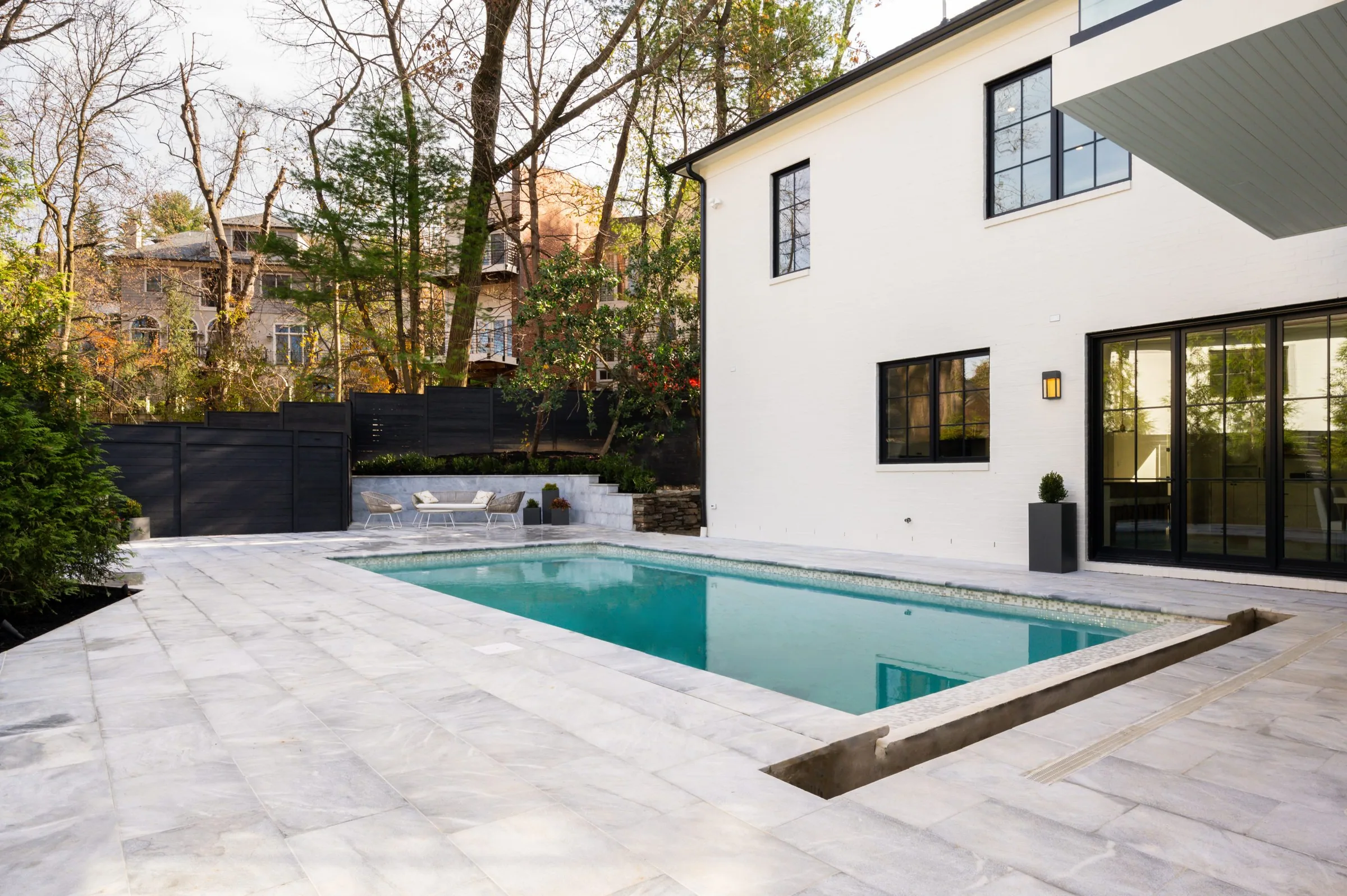 Custom backyard swimming pool surrounded by a stone patio and greenery