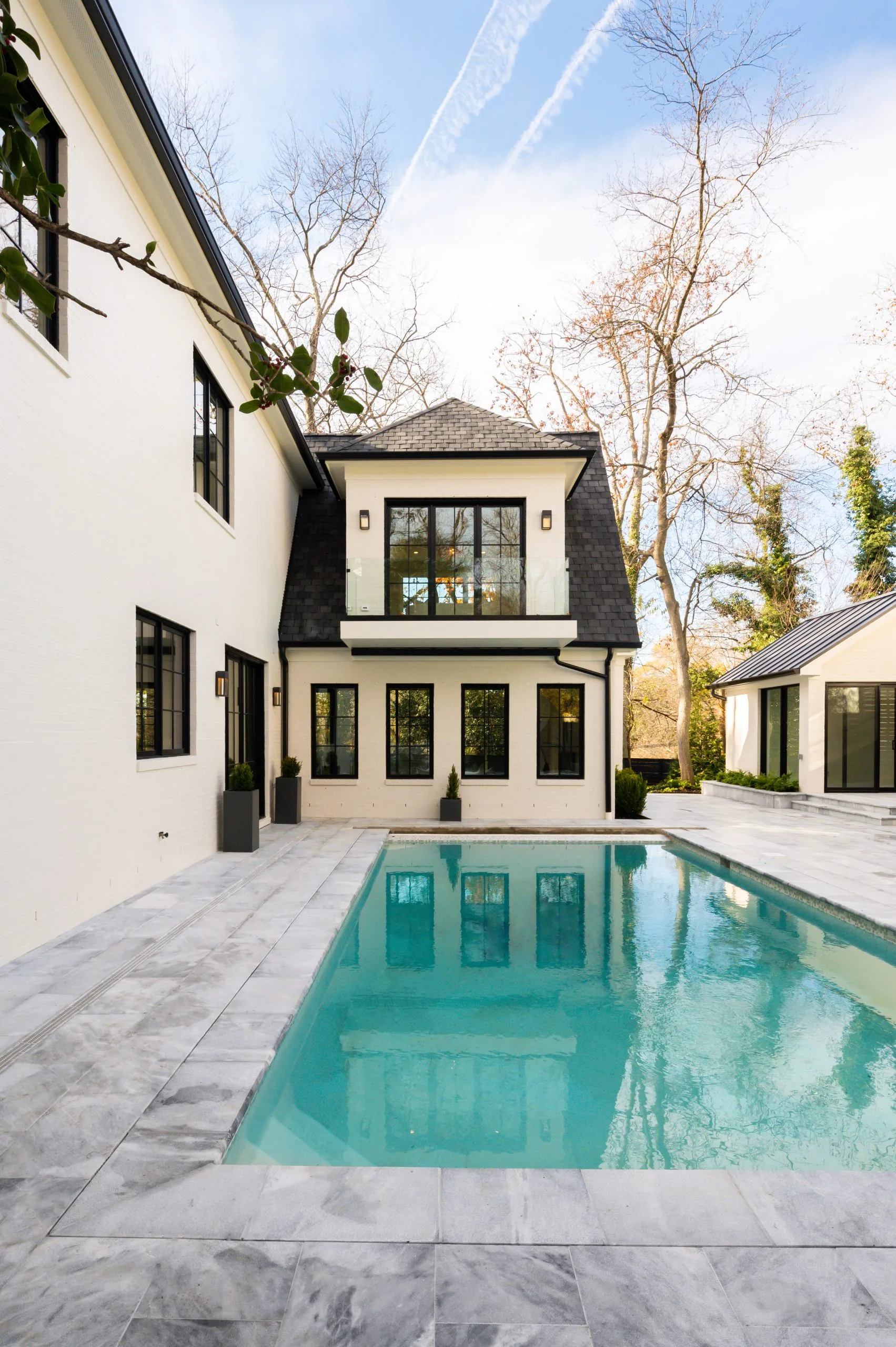 Narrow view along a pool beside a modern white house and pale stone patio