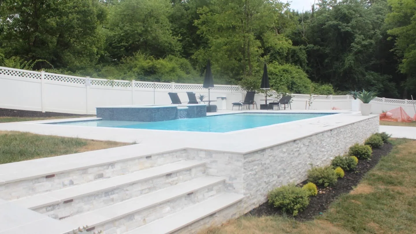 Stone steps and a raised patio beside a swimming pool and white privacy fence