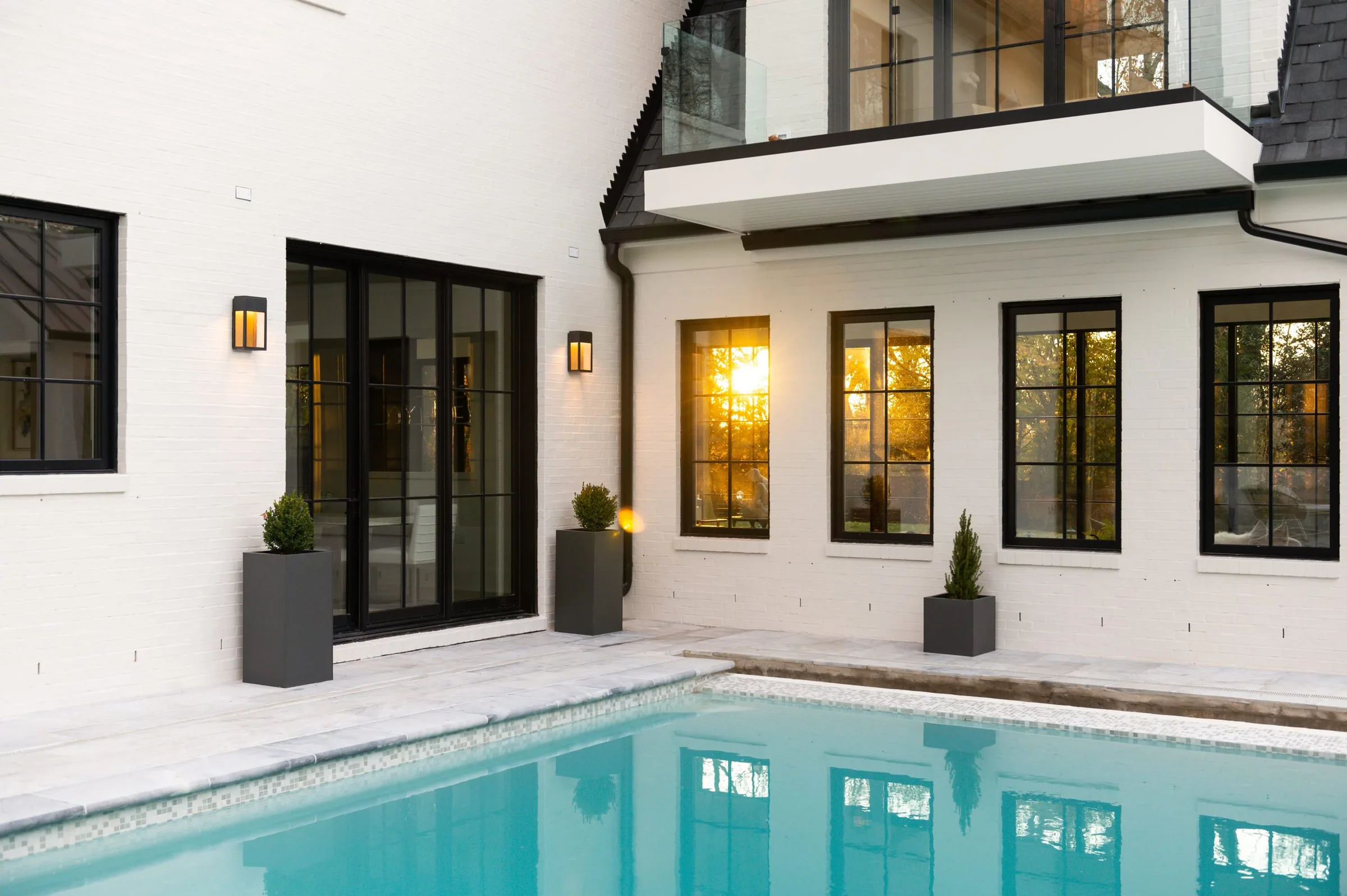 Pool reflecting the warm lights of a modern white house at dusk