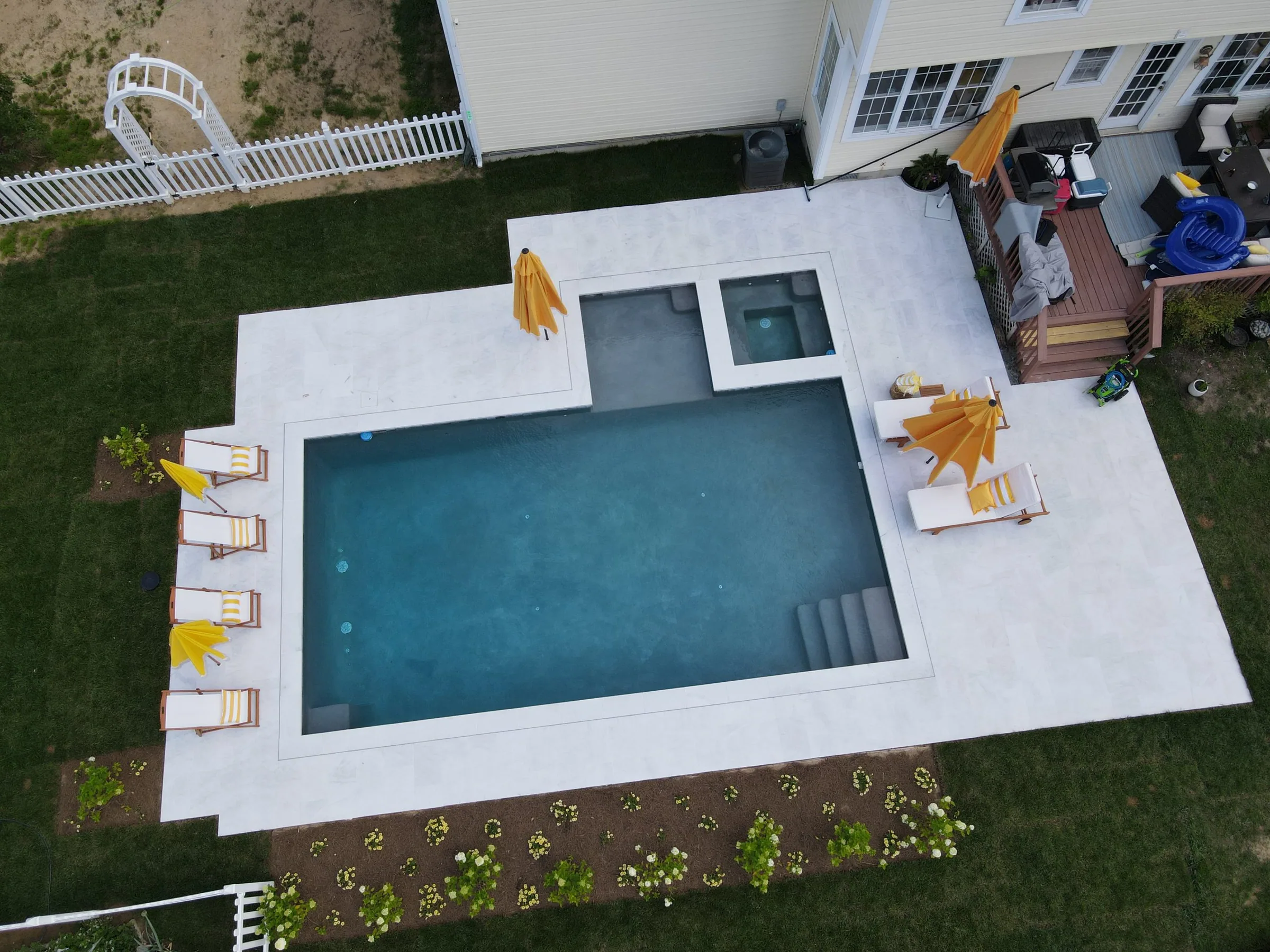 Overhead view of a pool and square spa with lounge chairs and umbrellas