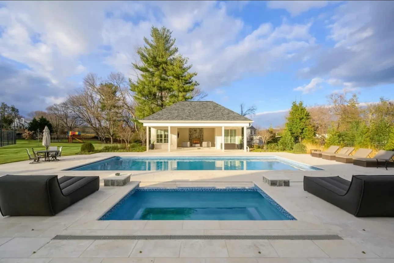 Swimming pool and square spa facing an open pool house with lounge seating