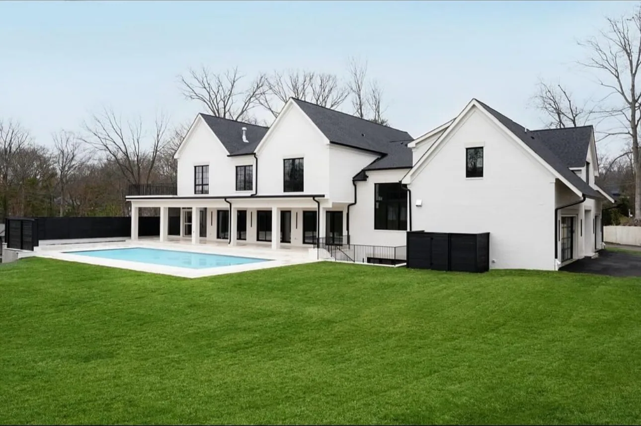 Pool terrace and a broad green lawn surrounding a white home