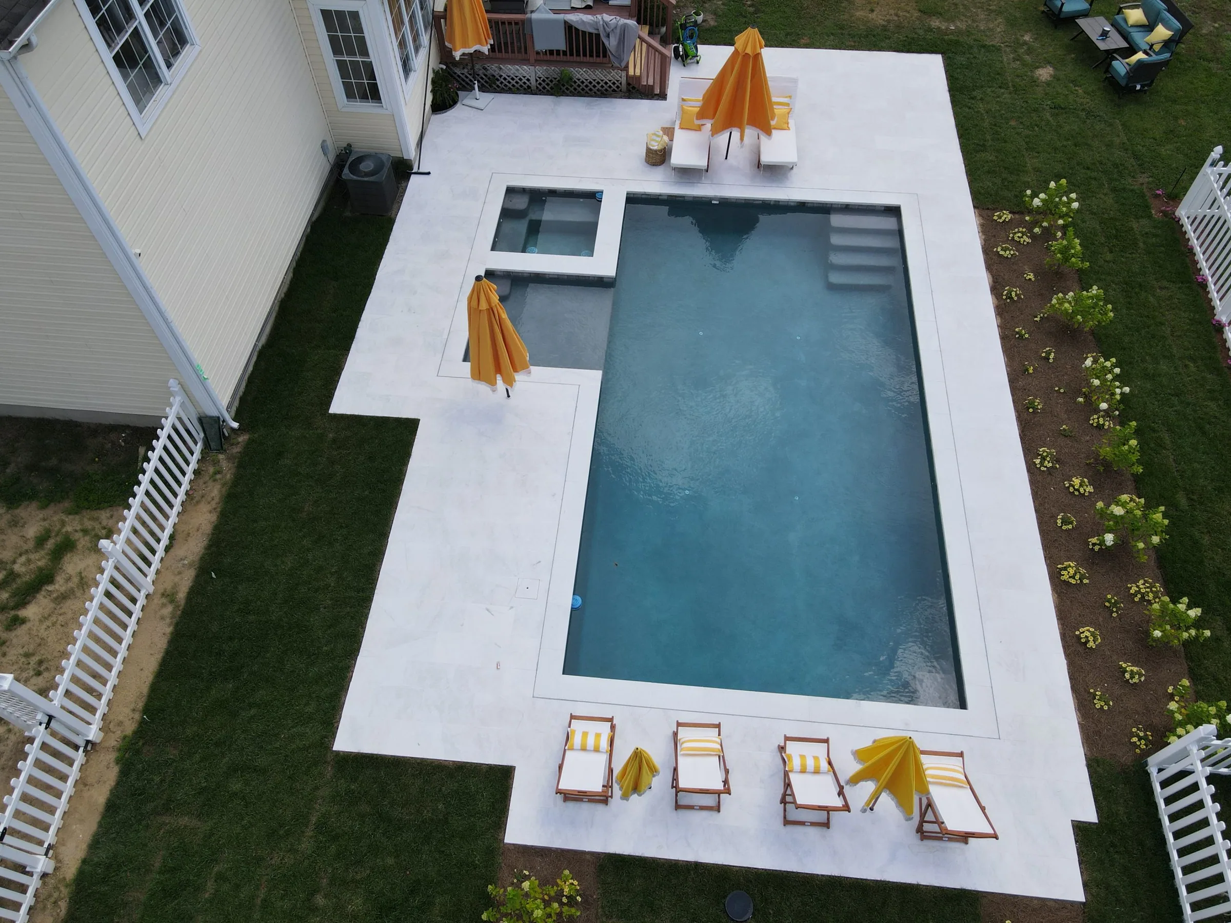 Overhead view of a rectangular pool and spa with a white patio and yellow umbrellas