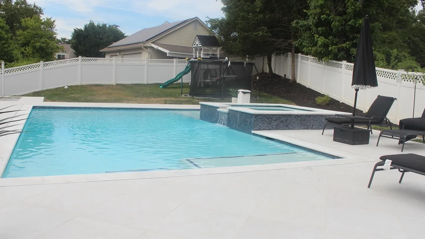 Blue swimming pool with a raised spa and sun shelf surrounded by pale stone paving