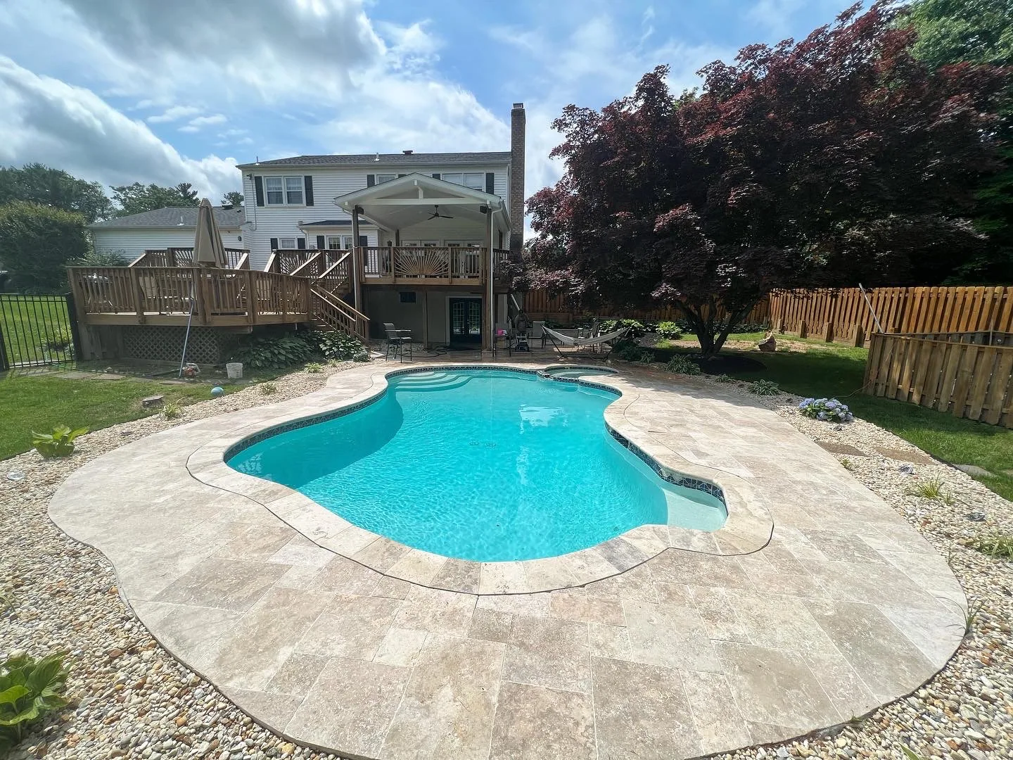 Freeform turquoise swimming pool with a stone surround in a landscaped backyard